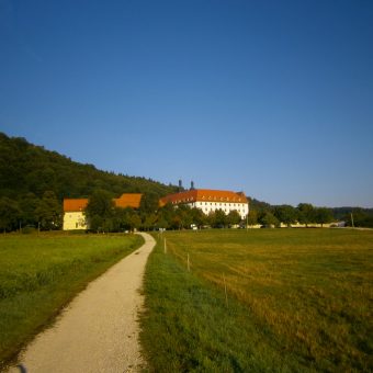 Schön gelegen an der Sonnenseite eines bewaldeten Tals liegt das alte Kloster, umgeben von ökologischen Viehweiden und Lindenbäumen. Die Barockanlage ist in einem Winkel von 120° gebaut, ähnlich wie die Bienenzelle.