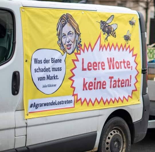 Politisches Banner eines Imkers auf seinem Imkerfahrzeug mit dem Portrait der Bundeslandwirtschafts-Ministerin und der Aufschrift: "Was der Biene schadet, muss vom Markt" und einer Biene, die sagt: "Leere Worte, keine Taten!"