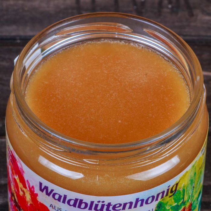Grossaufnahme eines geöffneten Honigglases mit bernsteinfarbenem, feinem Biohonig (bio-honig.com).