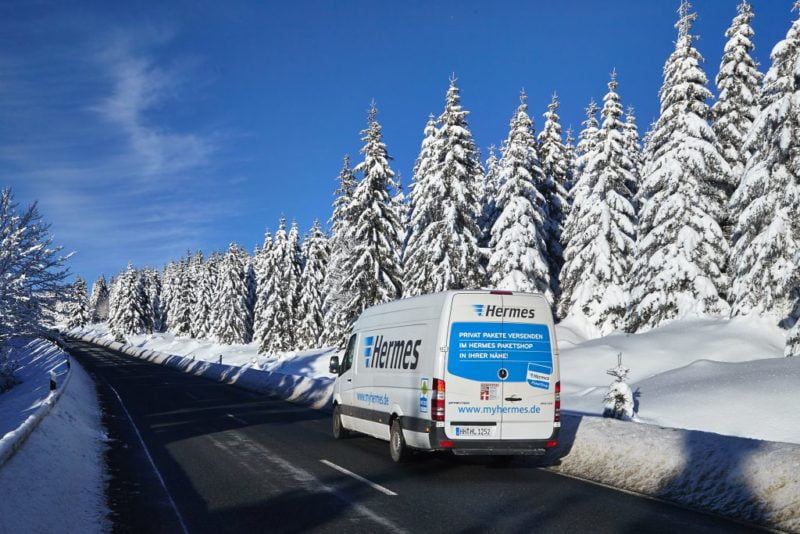 Paketfahrer unterwegs auf verschneiter Winterlandschaft.