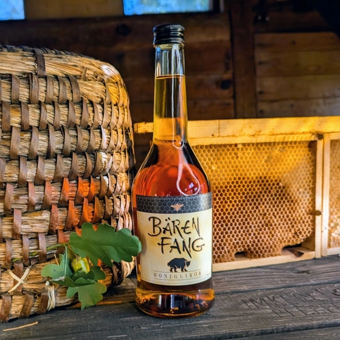 Eine Flasche ostpreussischer Bärenfang Honiglikör im Bienenhaus von Imkerei Oswald neben einem Bienenkorb und einer Bienenwabe. Foto: Hans Georg Oswald bio-honig.com