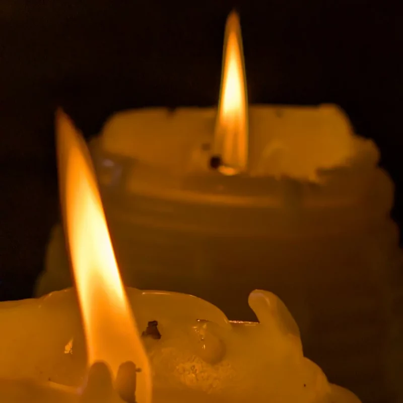 Zwei Flammen von brennenden Bienenwachskerzen in Bienenkorbgestalt in einem Bauernhaus in Bayern.
