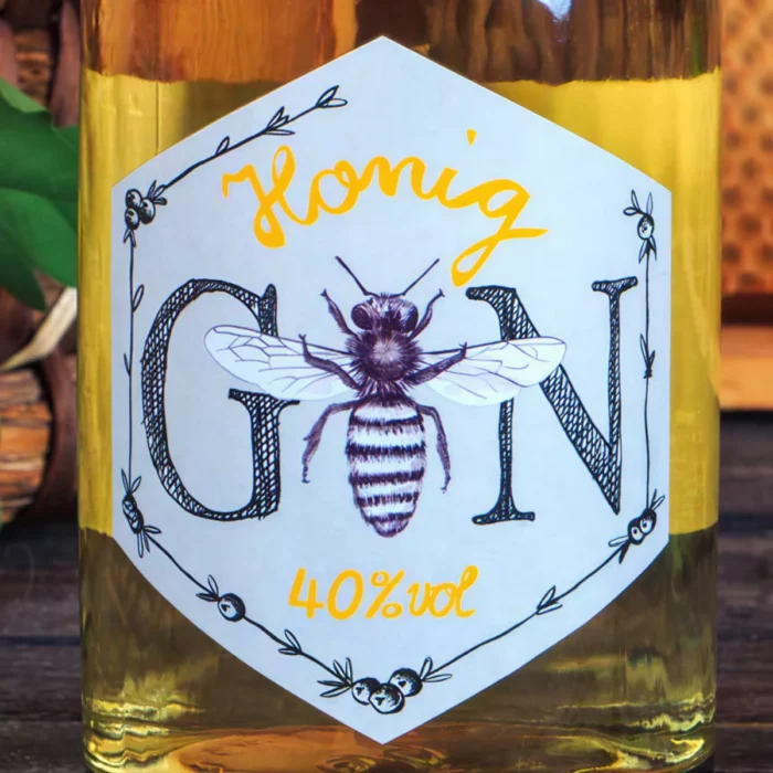 Gin Spirituose 0,5l, 40%vol | Honig-Gin vereint feine Aromen der Botanicals mit erlesenem Bienenhonig | Imkerei Oswald | Imkerei Oswald | bio-honig.com Gin Etikett Honig Gin 40% vol auf Cremepapier, stehendes Sechseck mit Honigbiene als Buchstabe "i", und handgezeichnete Randverzierung mit stilisierten Wacholderbeeren. Erhältlich im Online Versand Shop von Imkerei Oswald bio-honig com.