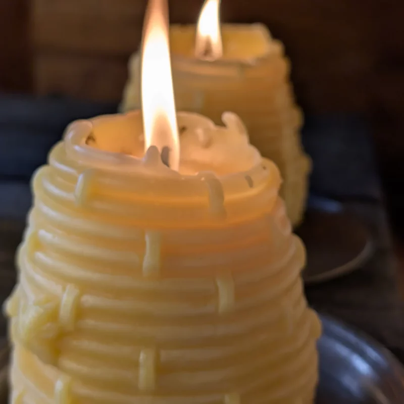 Zwei brennende Bienenwachskerzen in Bienenkorb Form auf jeweils einem Zinnteller als Untersatz in Bauernhaus in Bayern. Foto: Imkerei Oswald.