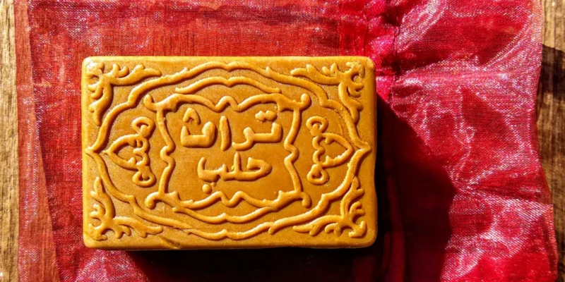 Goldbraune, kunstvoll geprägte Adlerbaumseife mit arabischer Kalligraphie und Ornamenten. Auf pupurotem Schmuckbeutel liegt diese traditionelle Oud-Seife. Foto: Hans Georg Oswald
