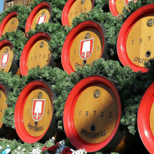 Festlich mit Tannengrün geschmückte Holzfässer der Spaten-Brauerei mit leuchtend roten Fassrändern auf einem traditionellen Festwagen.